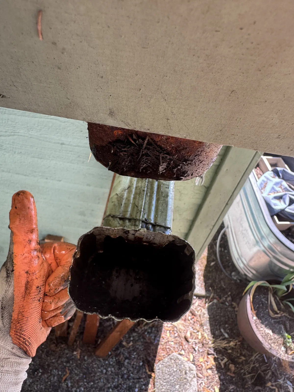 Same downspout elbow emptied of debris beside the green gutter, with a gloved thumbs up